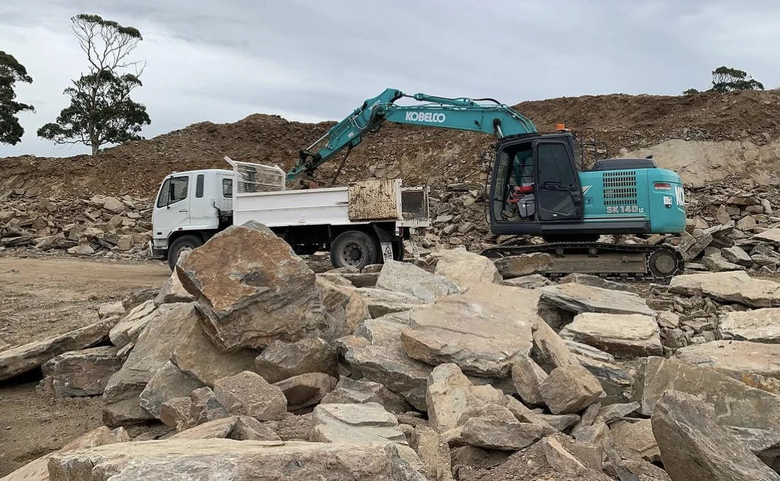 Valley excavator and tipper working among exposed rock on a site
