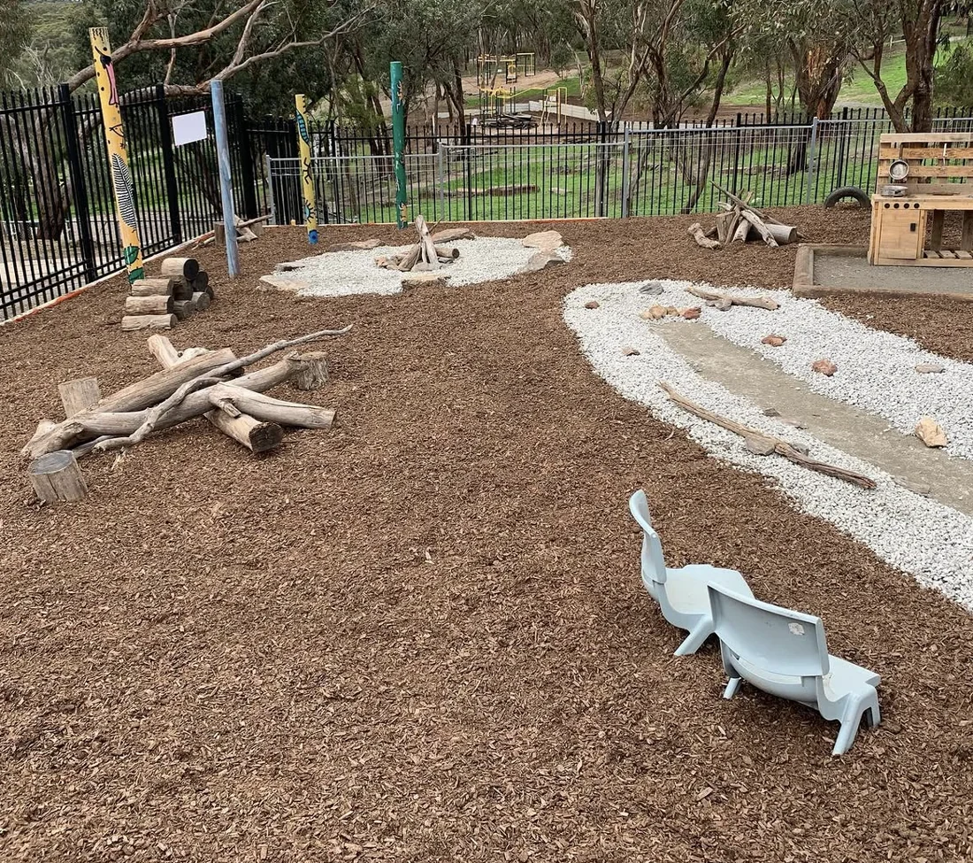 Outdoor nature play area with mulch, timber logs and winding gravel features